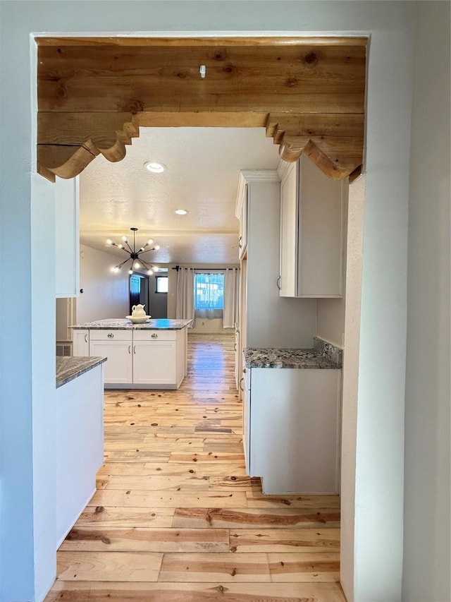 kitchen with kitchen peninsula, white cabinetry, light hardwood / wood-style flooring, and a notable chandelier