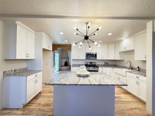 kitchen featuring appliances with stainless steel finishes, light wood-type flooring, light stone counters, sink, and white cabinets