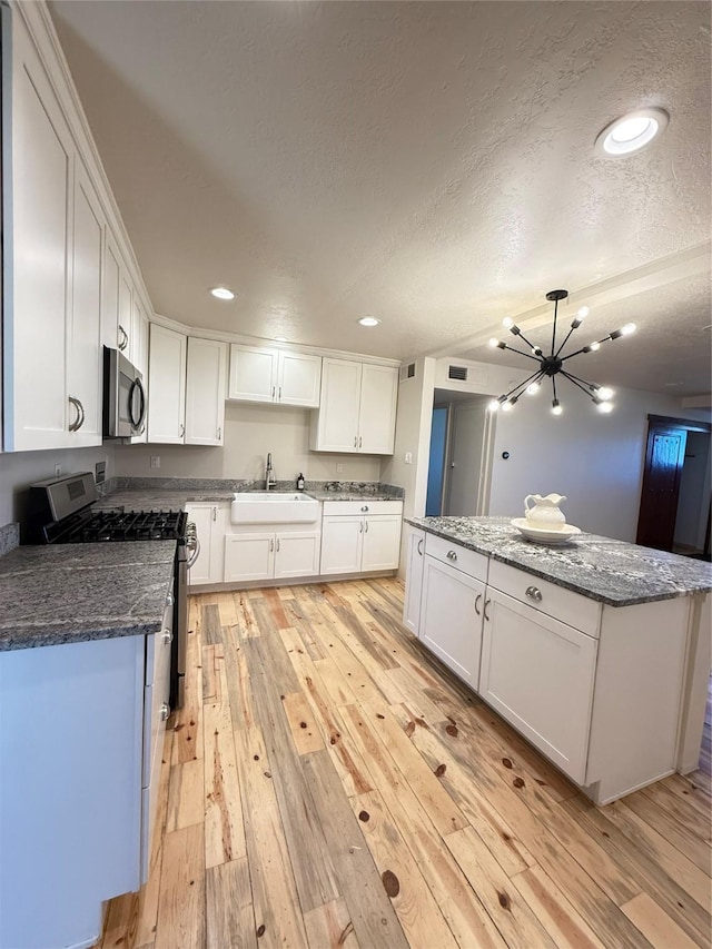 kitchen featuring sink, a chandelier, light hardwood / wood-style floors, white cabinets, and appliances with stainless steel finishes