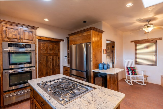 kitchen featuring ceiling fan, appliances with stainless steel finishes, light stone countertops, and a kitchen island