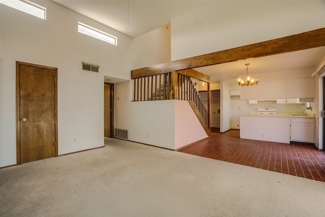 carpeted empty room featuring beamed ceiling, a towering ceiling, sink, and an inviting chandelier