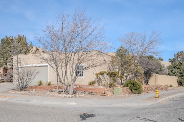 pueblo-style house featuring fence, driveway, an attached garage, and stucco siding