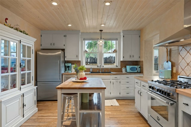 kitchen featuring wood counters, appliances with stainless steel finishes, wood ceiling, wall chimney range hood, and hanging light fixtures