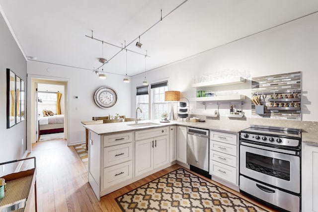 kitchen with light stone countertops, white cabinetry, sink, stainless steel appliances, and kitchen peninsula