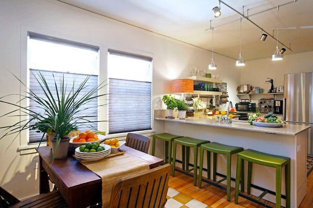 kitchen with sink, light wood-type flooring, decorative light fixtures, kitchen peninsula, and stainless steel refrigerator