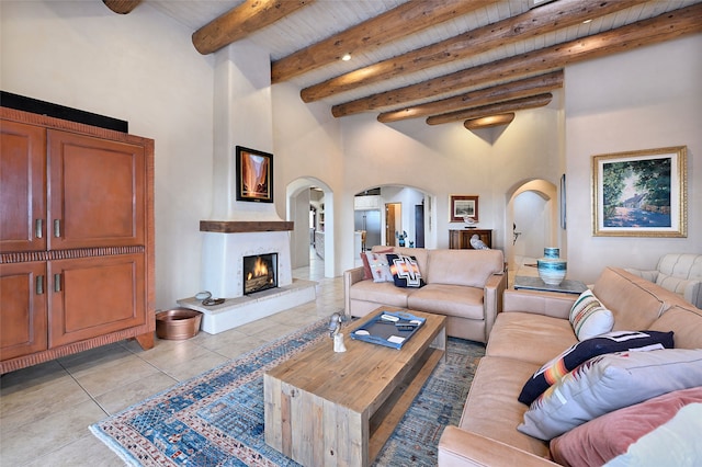 tiled living room featuring a towering ceiling, a large fireplace, beamed ceiling, and wooden ceiling