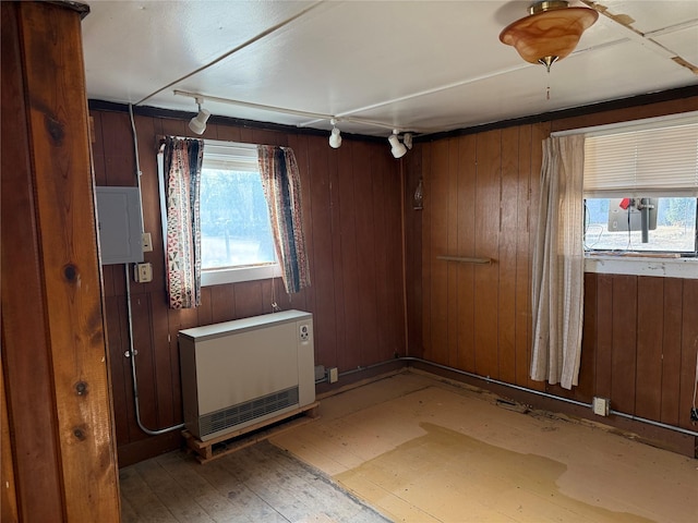 empty room featuring track lighting, electric panel, wooden walls, and heating unit