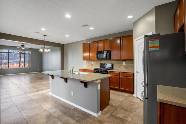 kitchen with black appliances, a center island with sink, decorative backsplash, decorative light fixtures, and a breakfast bar area