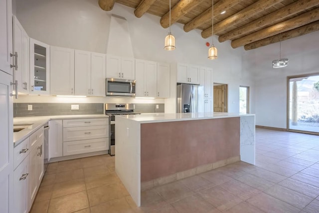 kitchen featuring stainless steel appliances, pendant lighting, white cabinets, and beamed ceiling