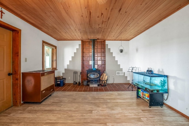 living room with light hardwood / wood-style floors, a wood stove, crown molding, and wood ceiling