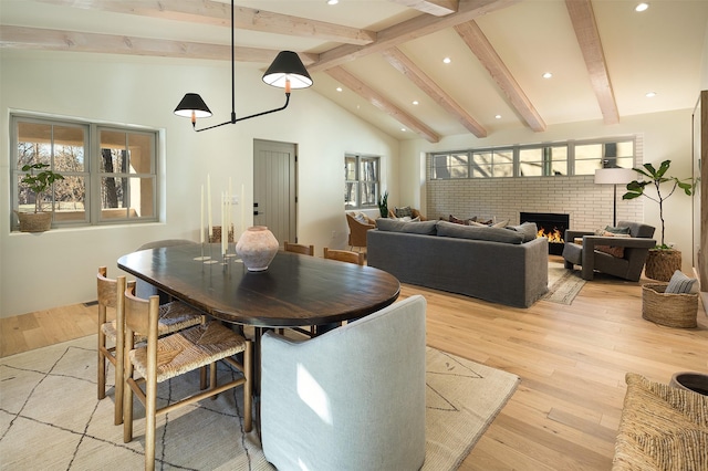 dining area with a brick fireplace, vaulted ceiling with beams, and light hardwood / wood-style flooring