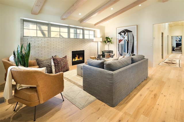 living room with vaulted ceiling with beams, light hardwood / wood-style floors, and a brick fireplace