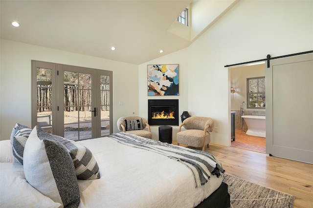 bedroom with light wood-type flooring, a barn door, access to outside, and ensuite bath