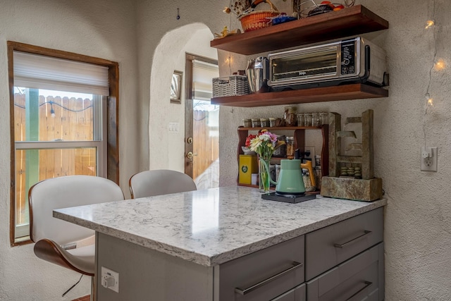 kitchen with gray cabinets, a wealth of natural light, and light stone countertops