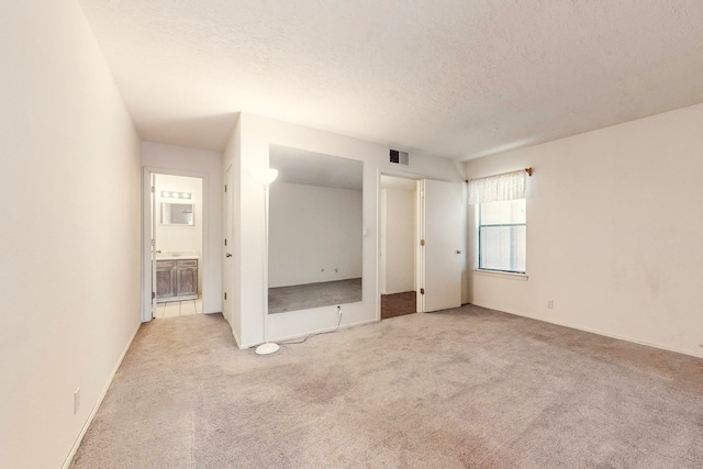 unfurnished bedroom with ensuite bathroom, light colored carpet, and a textured ceiling