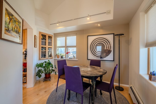 dining space featuring vaulted ceiling, baseboard heating, track lighting, and light hardwood / wood-style floors