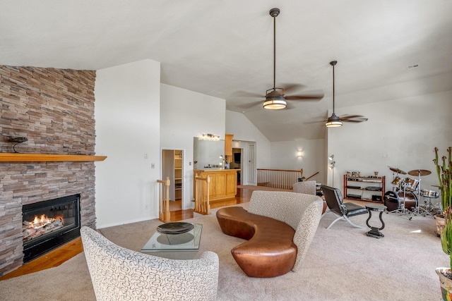 living room featuring light carpet, ceiling fan, vaulted ceiling, and a stone fireplace