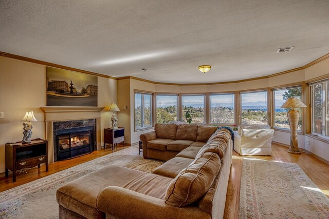 living room featuring ornamental molding, light wood-type flooring, a high end fireplace, and a textured ceiling