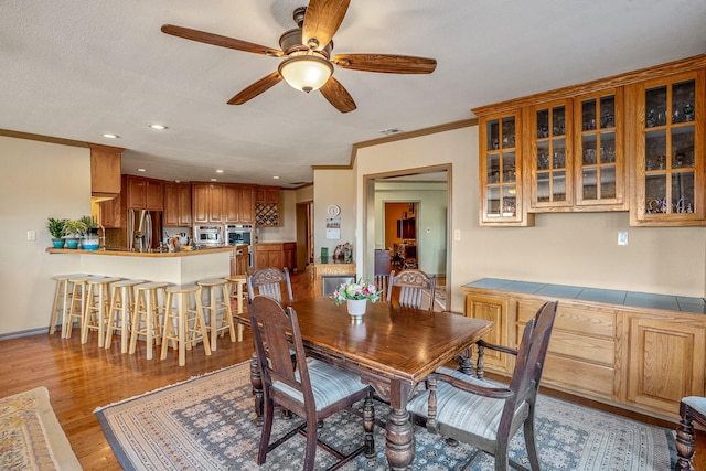 dining room with a textured ceiling, ceiling fan, light hardwood / wood-style floors, and ornamental molding