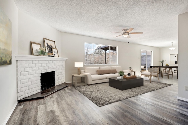 living room featuring a brick fireplace, a textured ceiling, ceiling fan, and hardwood / wood-style floors