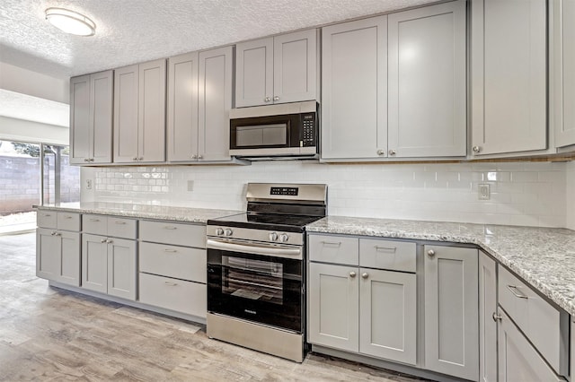 kitchen with gray cabinets, stainless steel appliances, light wood-type flooring, light stone countertops, and a textured ceiling