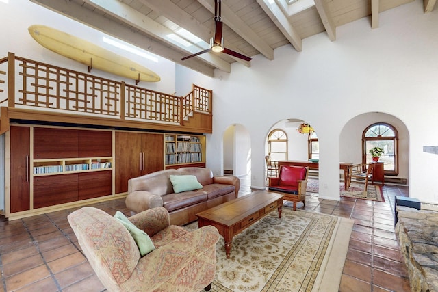 living room featuring wooden ceiling, a towering ceiling, beamed ceiling, ceiling fan, and built in features