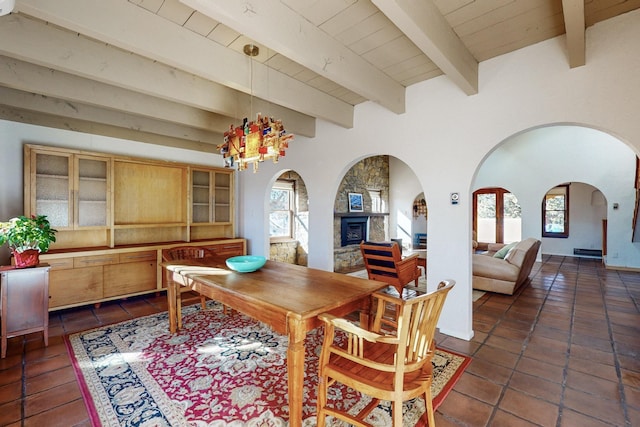 tiled dining area with wood ceiling, beam ceiling, a notable chandelier, and a stone fireplace