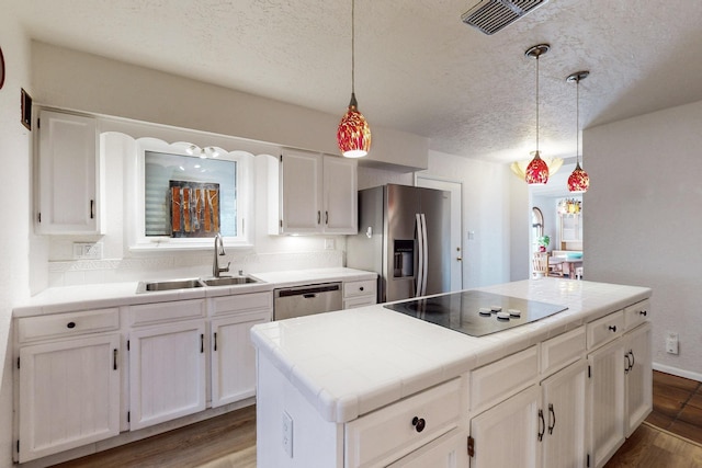 kitchen featuring appliances with stainless steel finishes, pendant lighting, tile countertops, a kitchen island, and sink