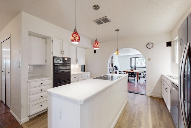 kitchen featuring decorative light fixtures, white cabinetry, a center island, hardwood / wood-style floors, and black appliances