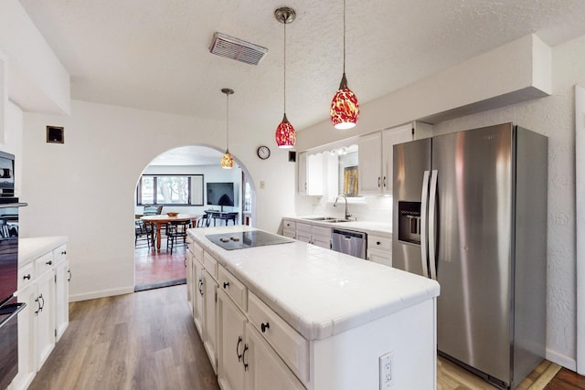 kitchen featuring hanging light fixtures, a center island, white cabinets, appliances with stainless steel finishes, and sink