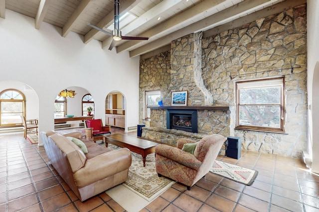 living room featuring a stone fireplace, a towering ceiling, ceiling fan, wood ceiling, and beam ceiling