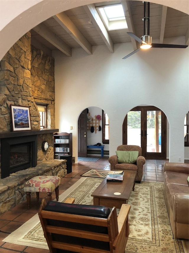 living room featuring wood ceiling, a stone fireplace, beamed ceiling, ceiling fan, and french doors