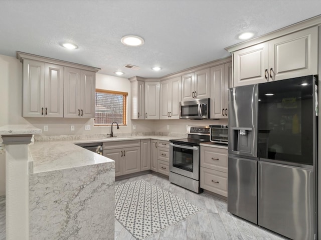 kitchen with light stone countertops, light wood-type flooring, appliances with stainless steel finishes, and sink