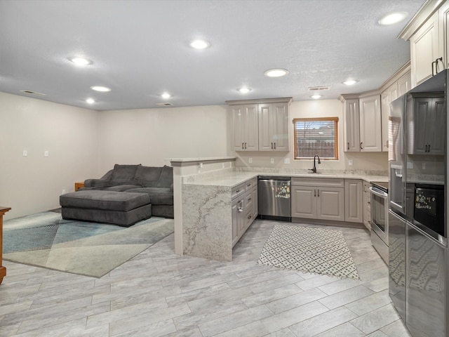 kitchen featuring kitchen peninsula, stainless steel appliances, light stone countertops, and sink