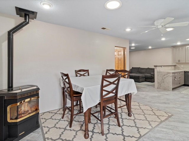 dining space with ceiling fan and a wood stove