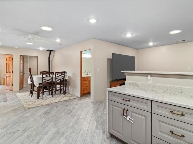 kitchen with gray cabinetry, ceiling fan, light hardwood / wood-style floors, and light stone countertops