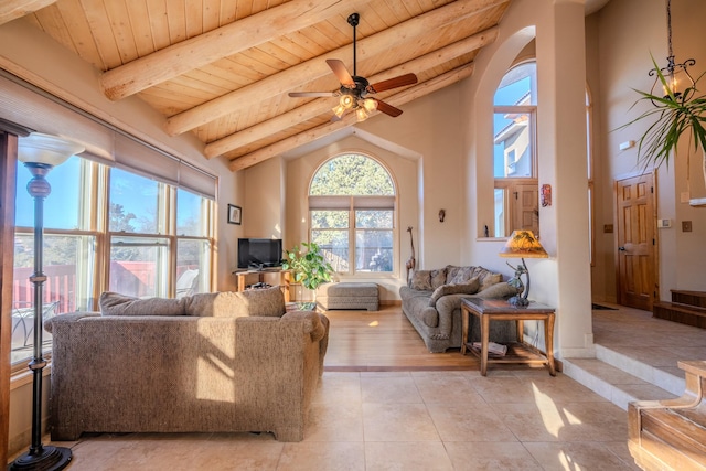 living area with arched walkways, a ceiling fan, light tile patterned flooring, wooden ceiling, and beamed ceiling