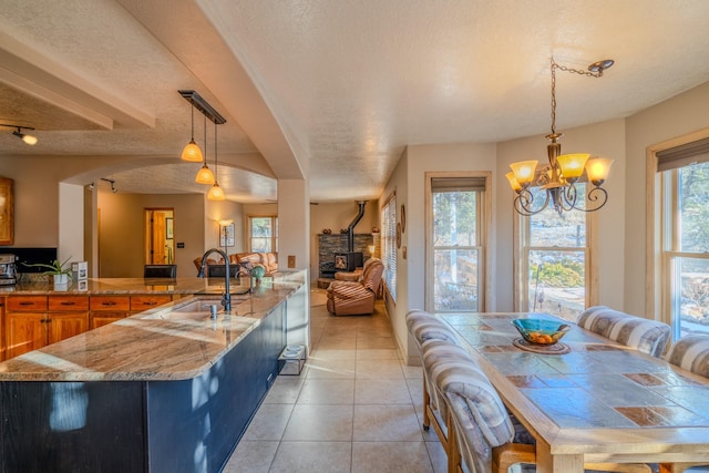 kitchen featuring light tile patterned floors, a textured ceiling, a sink, and a wood stove