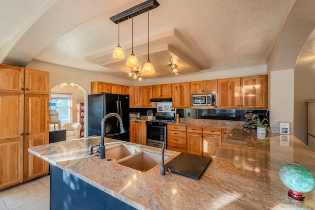 kitchen with a textured ceiling, light stone counters, stainless steel appliances, a peninsula, and decorative light fixtures