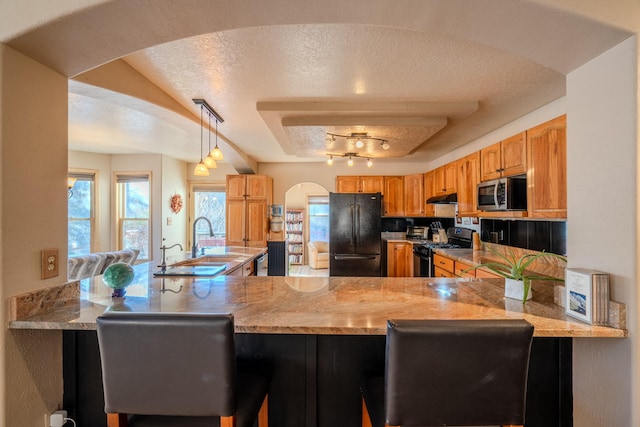 kitchen featuring arched walkways, a textured ceiling, a peninsula, under cabinet range hood, and black appliances