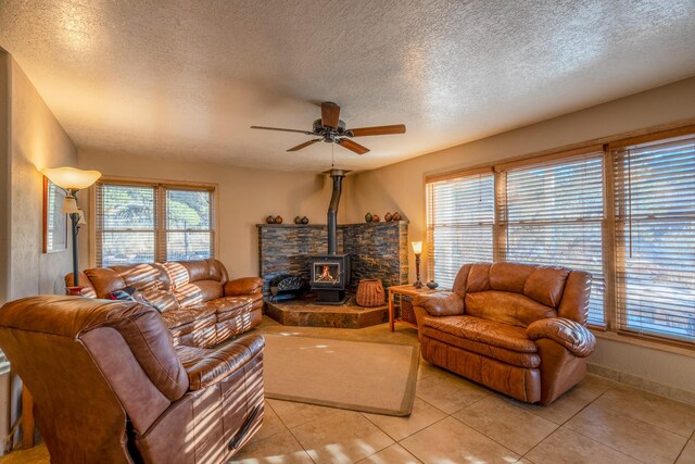 living area featuring light tile patterned floors, a textured ceiling, a ceiling fan, baseboards, and a wood stove