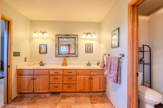 full bath with double vanity, a sink, toilet, and stone finish flooring