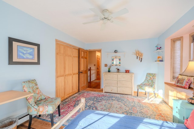 bedroom with a baseboard heating unit, a ceiling fan, a closet, and wood finished floors