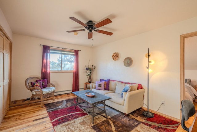 living area featuring a baseboard heating unit, light wood-type flooring, baseboards, and a ceiling fan