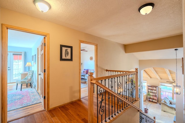 corridor featuring baseboards, lofted ceiling with beams, wood finished floors, a textured ceiling, and an upstairs landing