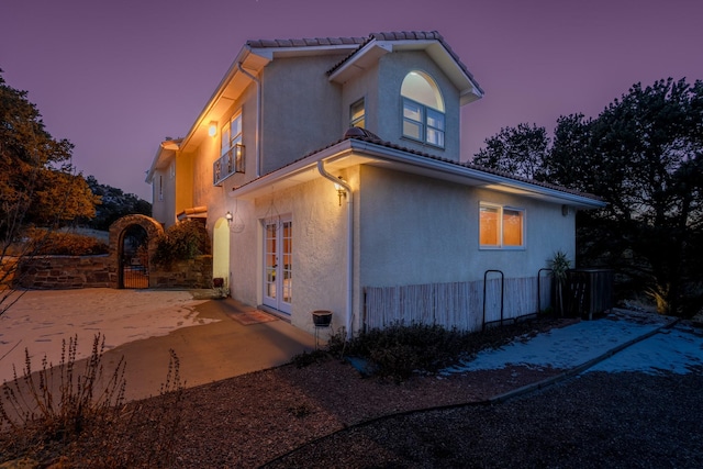 property exterior at dusk featuring stucco siding, a patio area, fence, and french doors