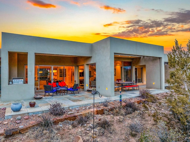 back house at dusk featuring a patio area and an outdoor living space with a fire pit