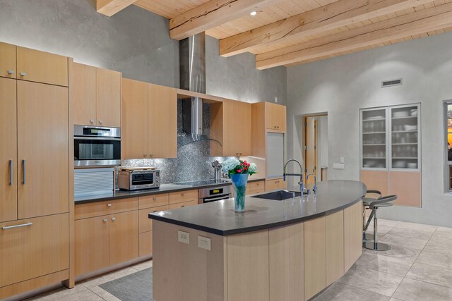 kitchen featuring wooden ceiling, a kitchen island with sink, stainless steel oven, beamed ceiling, and sink