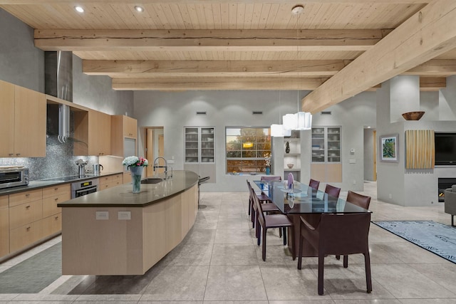 kitchen featuring light brown cabinetry, decorative light fixtures, oven, decorative backsplash, and a kitchen island with sink