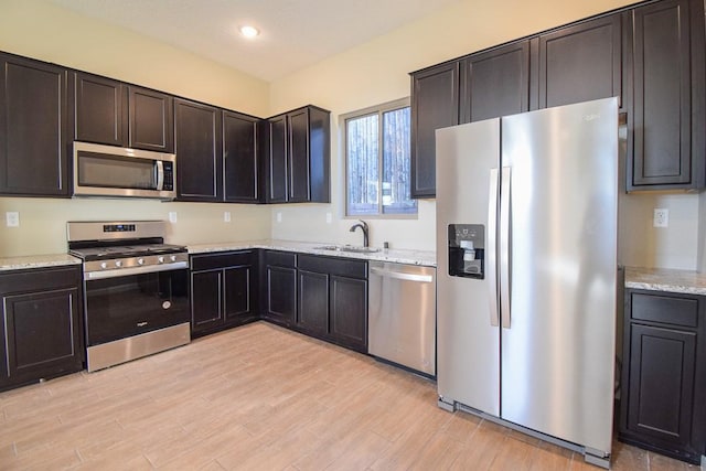 kitchen with appliances with stainless steel finishes, light wood-type flooring, light stone counters, dark brown cabinetry, and sink